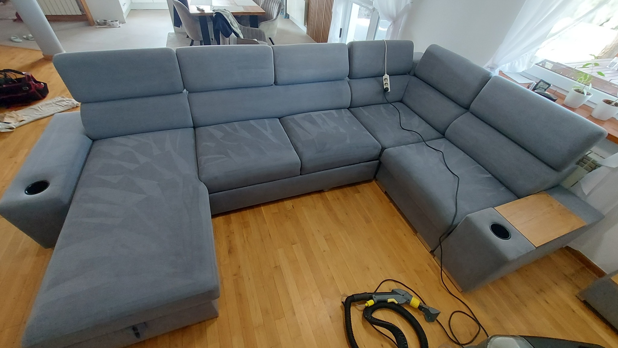 Szary, modułowy narożnik z widocznymi śladami czyszczenia na siedziskach i oparciach, obok leży odkurzacz piorący z końcówką do tapicerki.