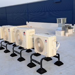 AEROKLIM Oleksandr Bashov - Rząd kremowych jednostek zewnętrznych klimatyzacji marki Gree, zamontowanych na czarnych metalowych podstawach na płaskim dachu budynku z niebieską fasadą.