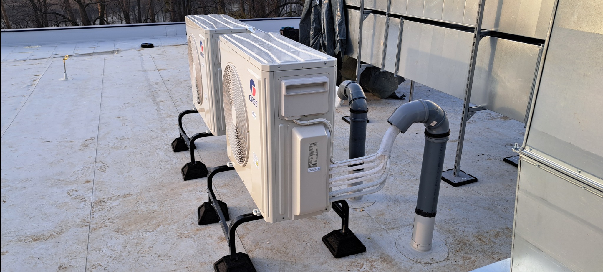 Dwa klimatyzatory marki Gree zamontowane na dachu, z widocznymi rurami odprowadzającymi skropliny i elementami wentylacji.