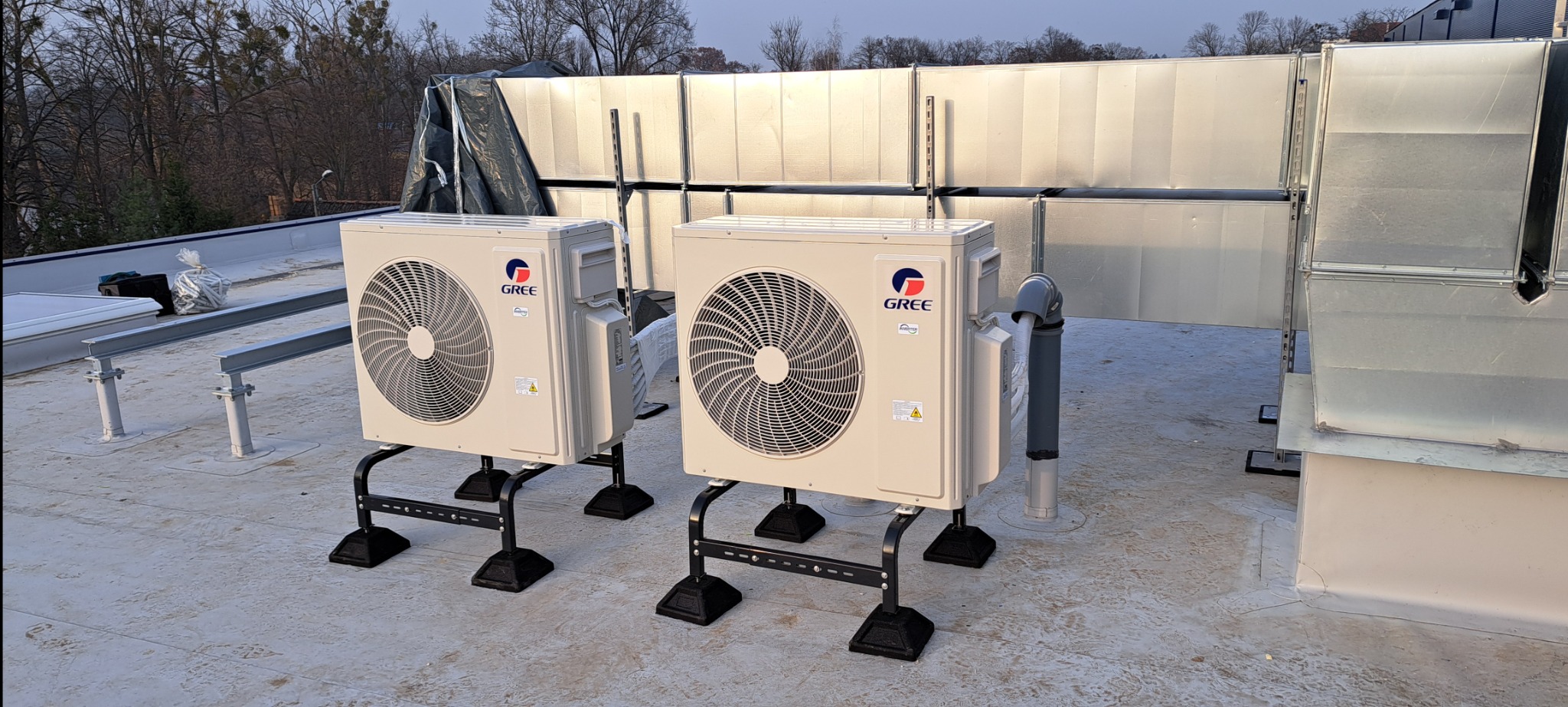 Dwa klimatyzatory marki Gree zamontowane na dachu płaskim, widoczne kanały wentylacyjne w tle.