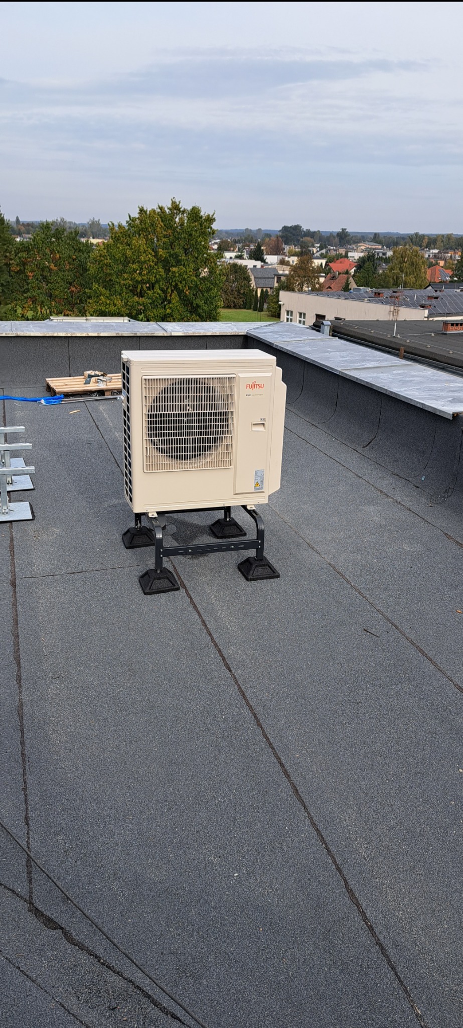 Zewnętrzna jednostka klimatyzacji Fujitsu zamontowana na dachu budynku z widokiem na zabudowania w tle.