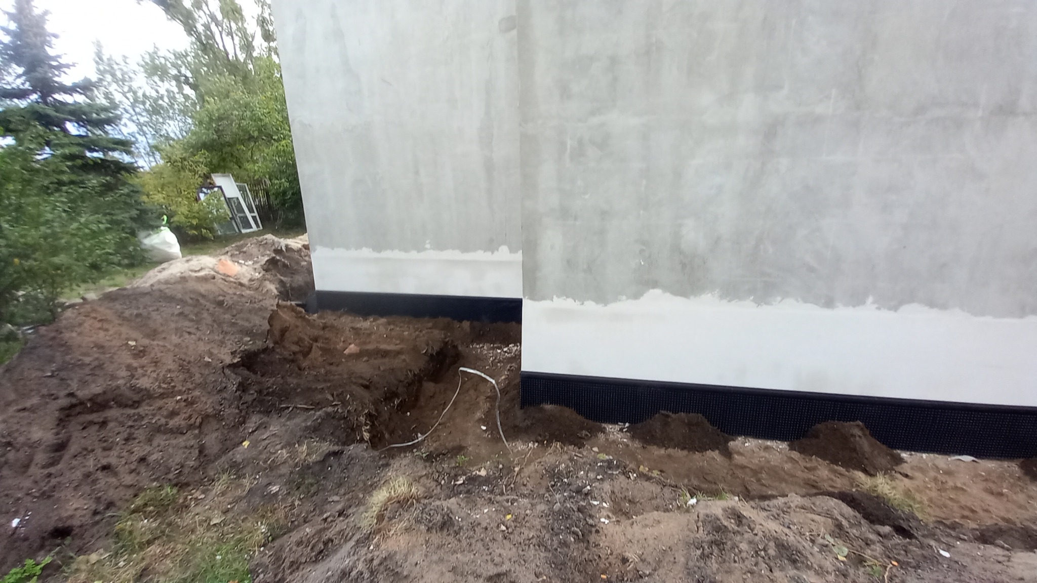 Fundament budynku z widoczną izolacją pionową i przygotowanym wykopem pod drenaż.