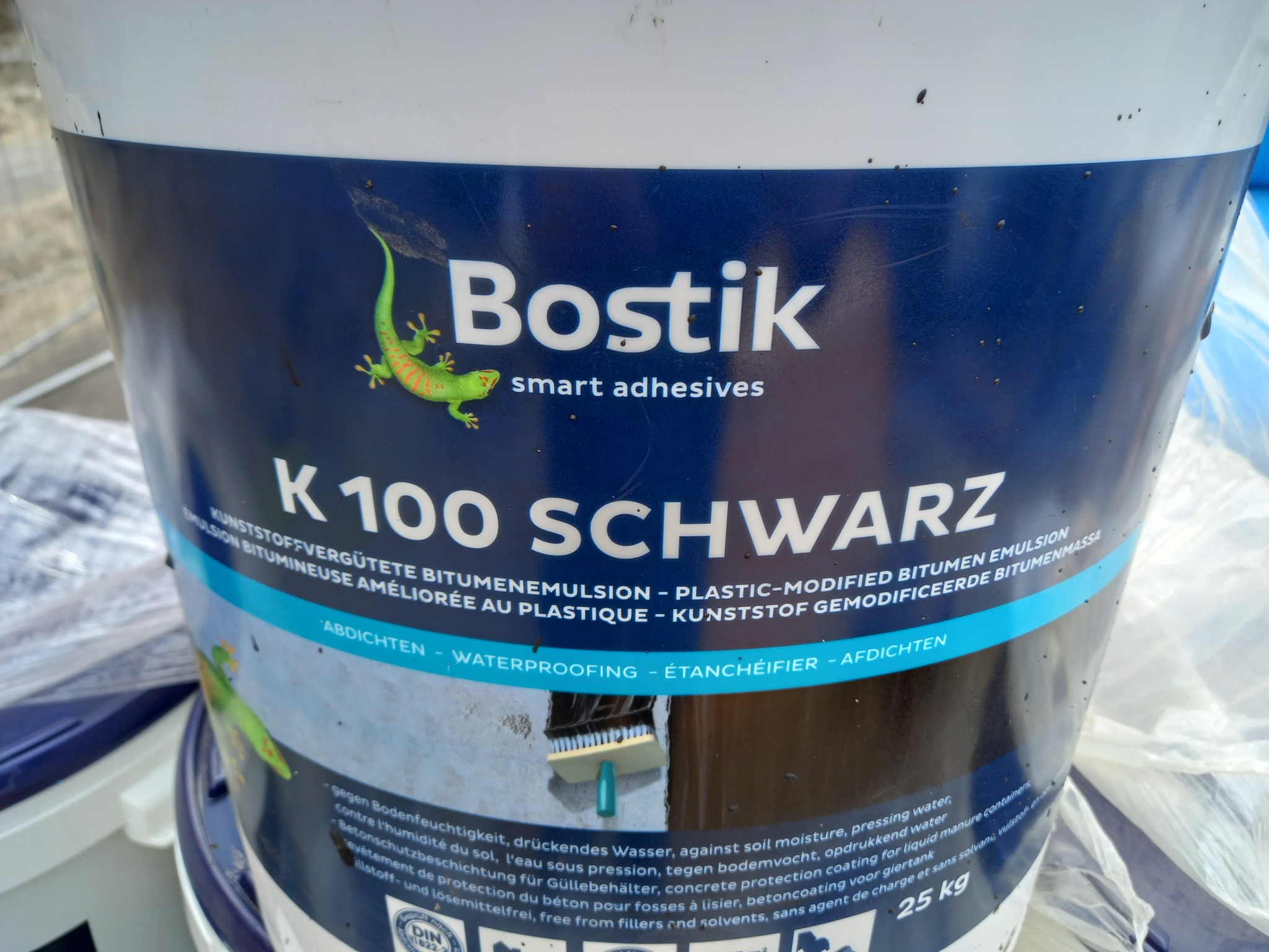 Wiadro z bitumiczną emulsją Bostik K100 Schwarz do hydroizolacji, z widocznym logo firmy i oznaczeniami właściwości produktu, lekko zabrudzone.