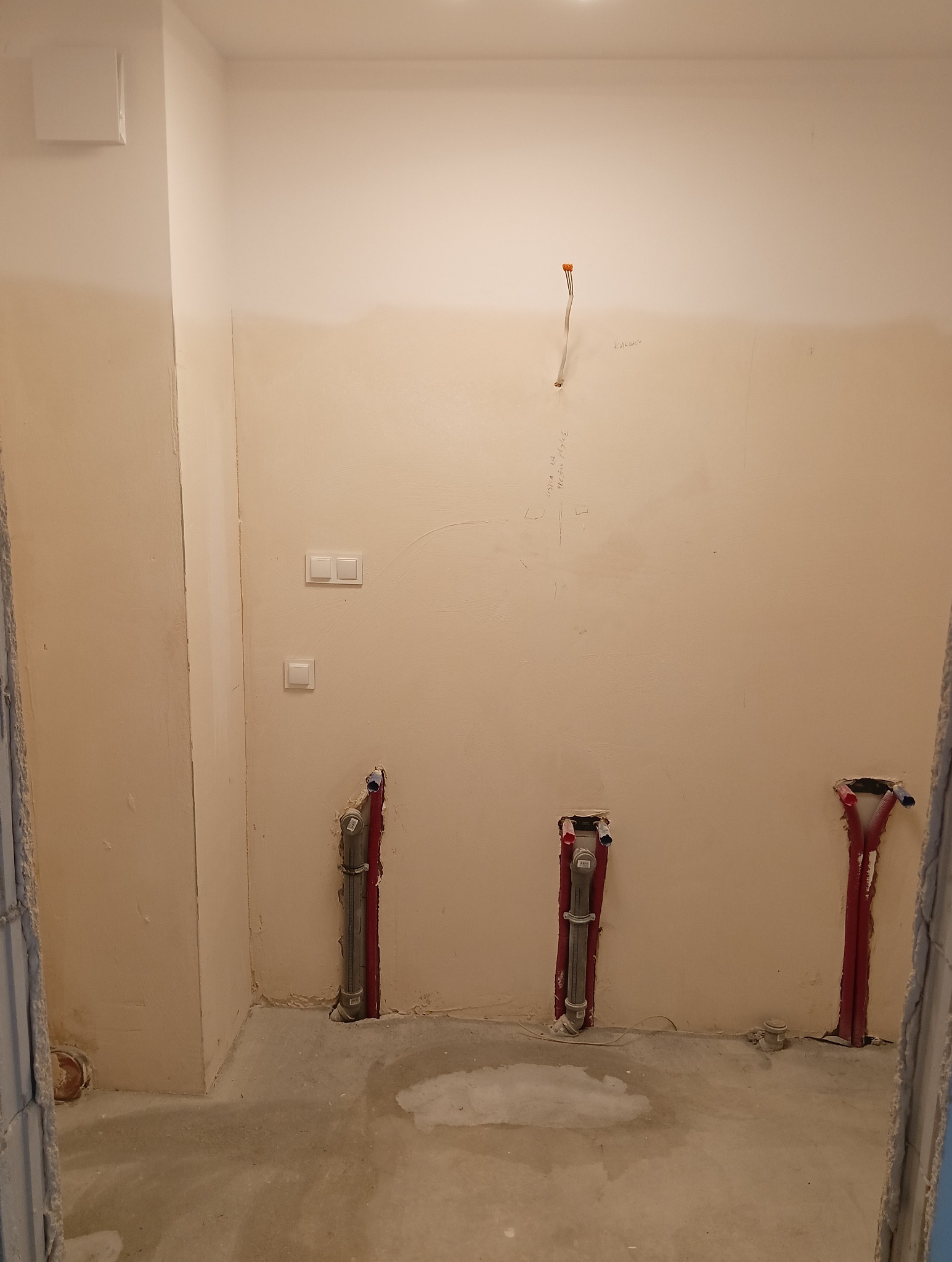 Surowy stan łazienki w Proszkowicach przed remontem: widoczne wyprowadzone rury instalacji wodnej i kanalizacyjnej w ścianie, zamontowane nowe włączniki światła, ściany przygotowane do malowania...