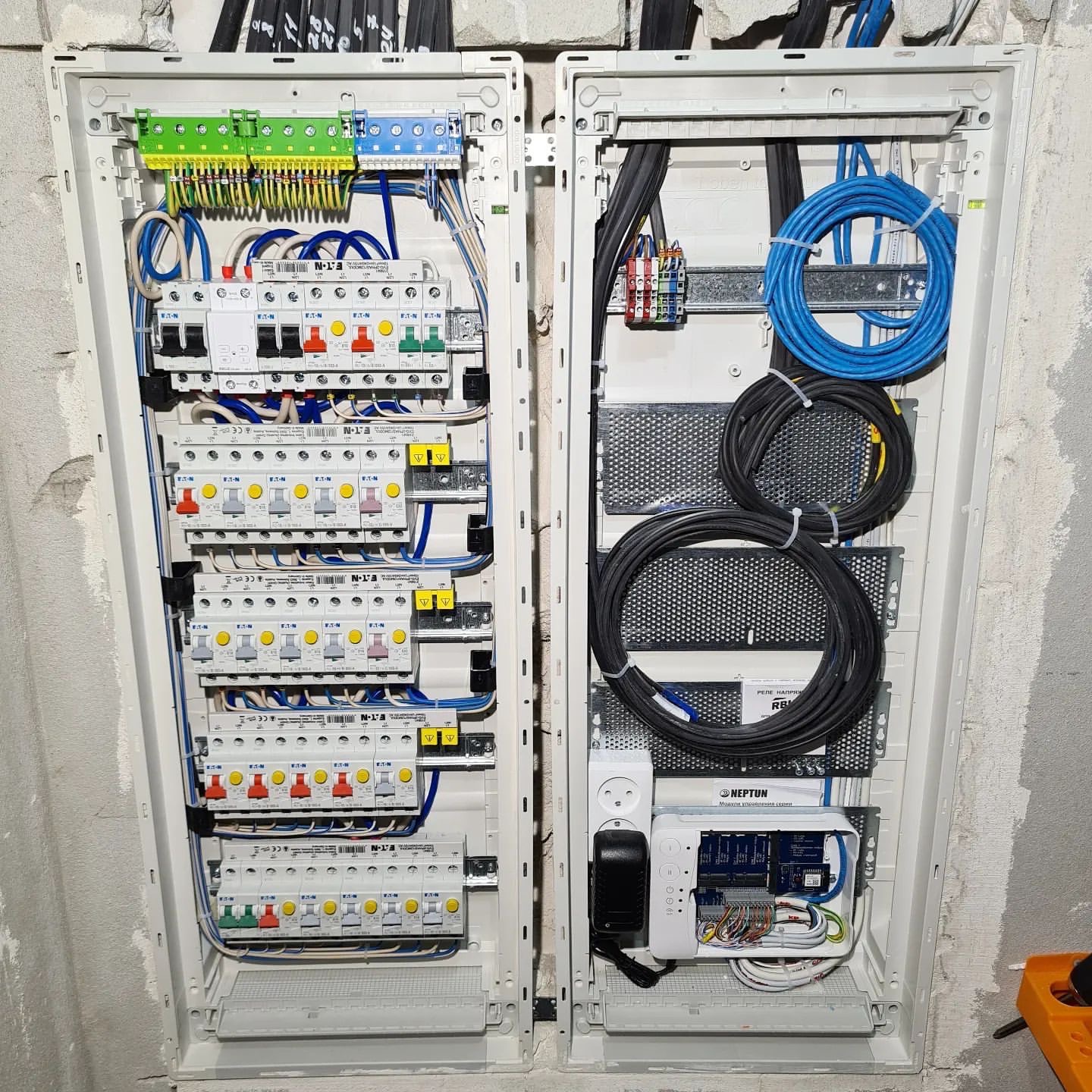 Dwa panele rozdzielcze z okablowaniem, bezpiecznikami i modułem sterującym Neptun, zamontowane na surowej ścianie.