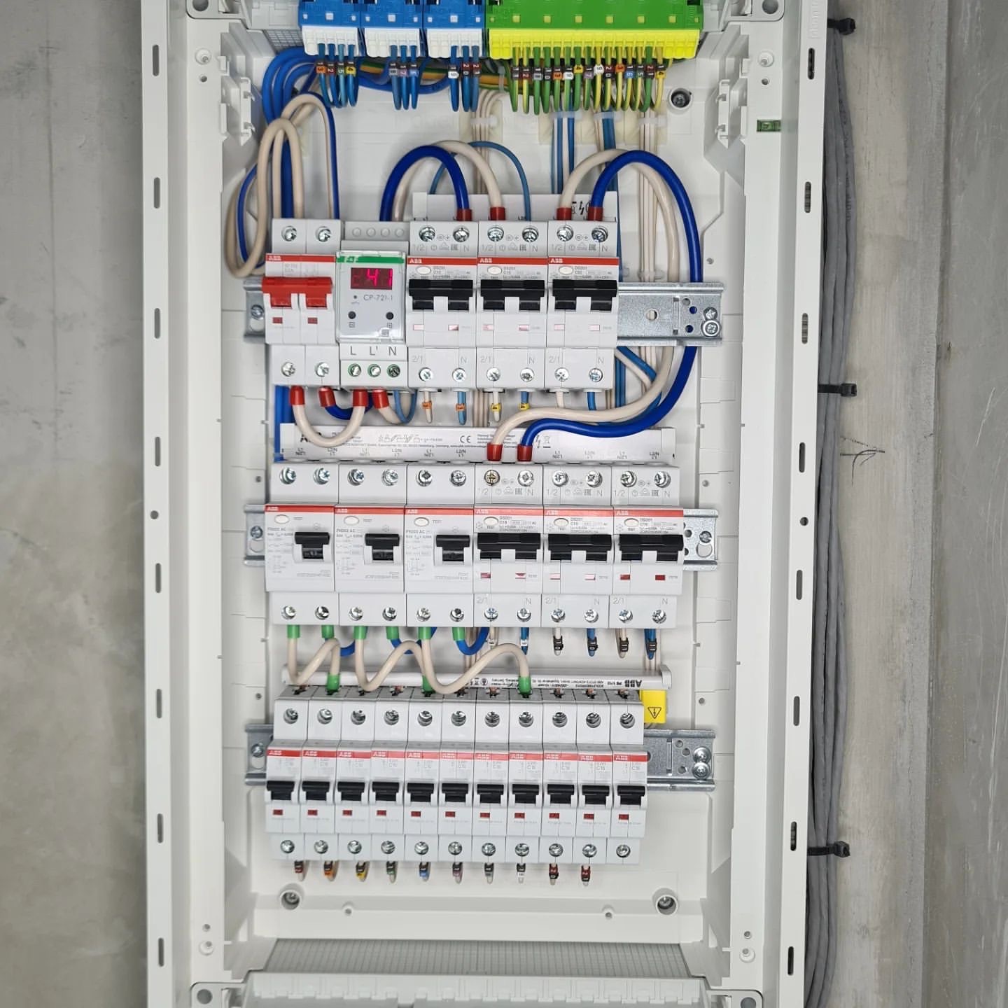 Rozdzielnica elektryczna z zainstalowanymi bezpiecznikami i przewodami, widoczne różne kolory przewodów i oznaczenia na urządzeniach, montaż w surowym wnętrzu.