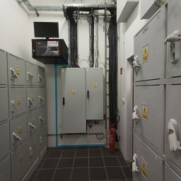 InstElectPro Andrii Dovhan - Wnętrze pomieszczenia z szafami elektrycznymi, rozdzielnicą, kablami prowadzonymi w korytach oraz gaśnicą w rogu, monitor i serwer na szafkach po lewej stronie.