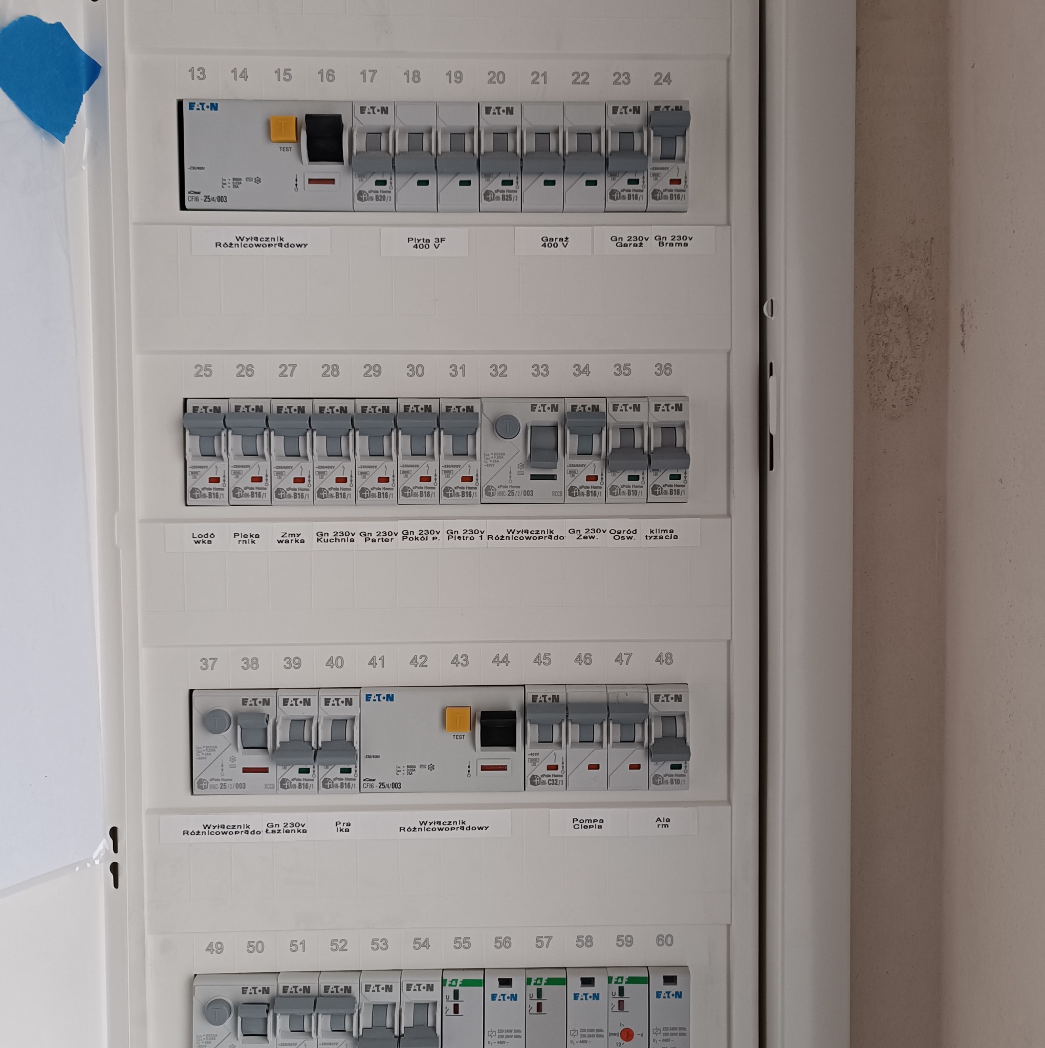 Szczegółowy widok skrzynki rozdzielczej z bezpiecznikami Eaton, zawierającej wyłączniki różnicowoprądowe i standardowe, z opisami obwodów, takimi jak 'Lodówka', 'Piekarnik', 'Płyta 3F 400V'...