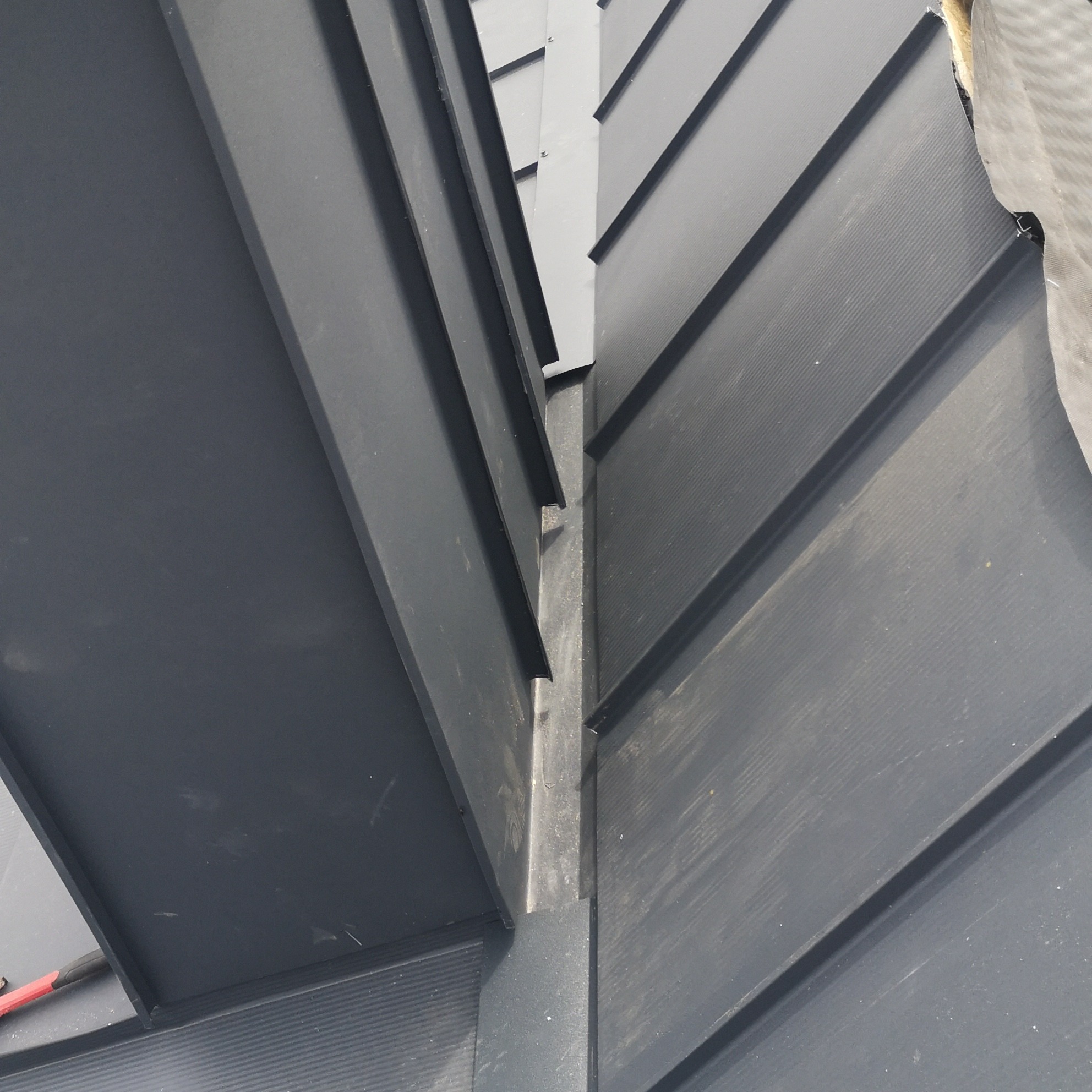 Szczegółowe ujęcie łączenia blach trapezowych na dachu, widoczne elementy mocujące i struktura blachy w antracytowym odcieniu.