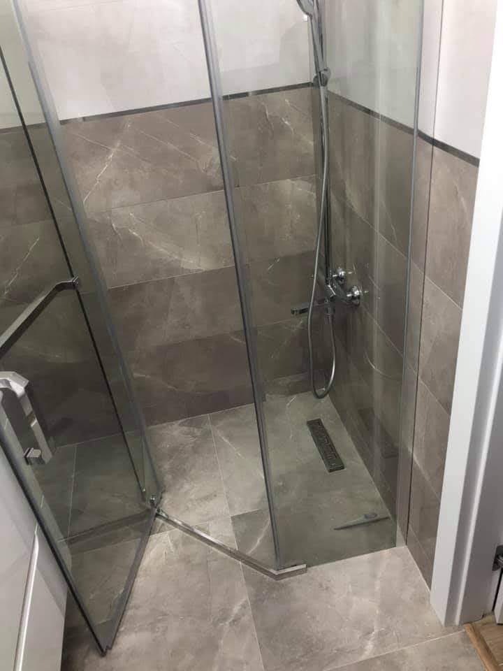 Nowoczesna kabina prysznicowa z szarymi płytkami imitującymi marmur, widoczny odpływ liniowy i chromowana armatura.