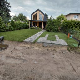 Paweł Machoniak - Nowoczesny dom z ogrodem po założeniu trawnika z rolki i ścieżki z kamienia. Widoczne elementy nawadniania. Pochmurne niebo.