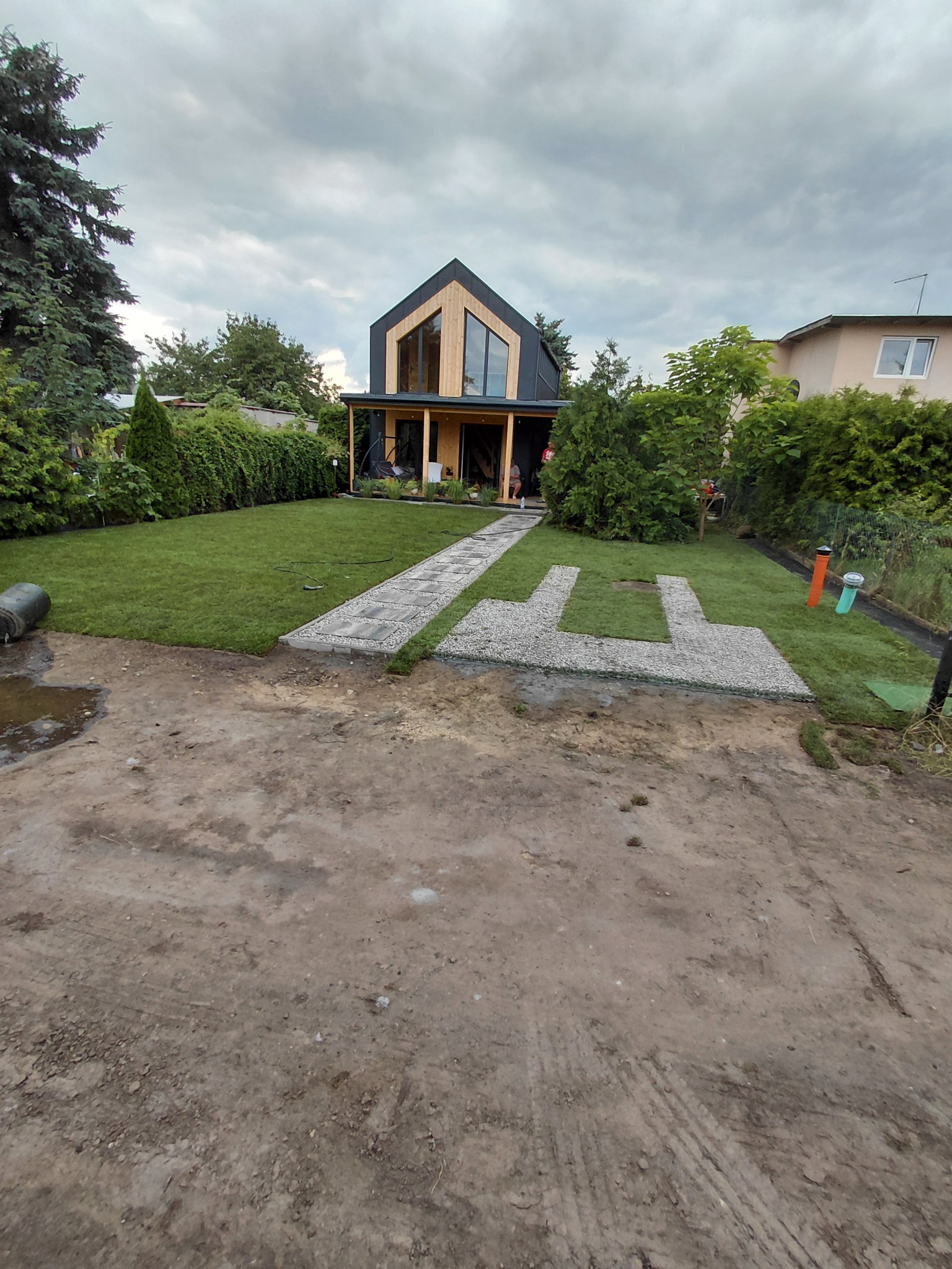 Nowoczesny dom z ogrodem po założeniu trawnika z rolki i ścieżki z kamienia. Widoczne elementy nawadniania. Pochmurne niebo.
