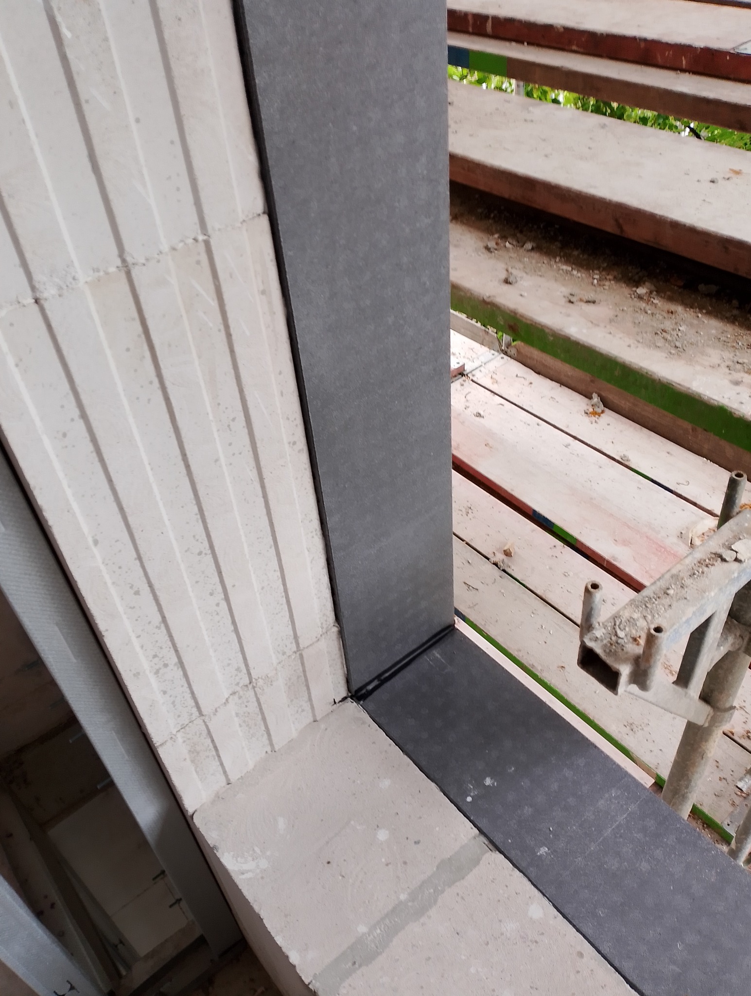 Fragment muru z betonu komórkowego z zamontowanym ościeżem drzwiowym w trakcie montażu, widoczne rusztowanie z boku.