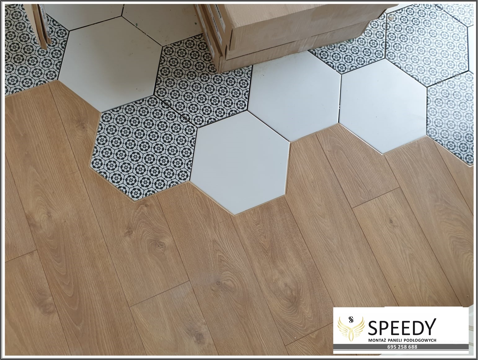 Połączenie podłogi z paneli drewnopodobnych i heksagonalnych płytek ceramicznych w białe i wzorzyste mozaiki, widoczny karton w rogu.