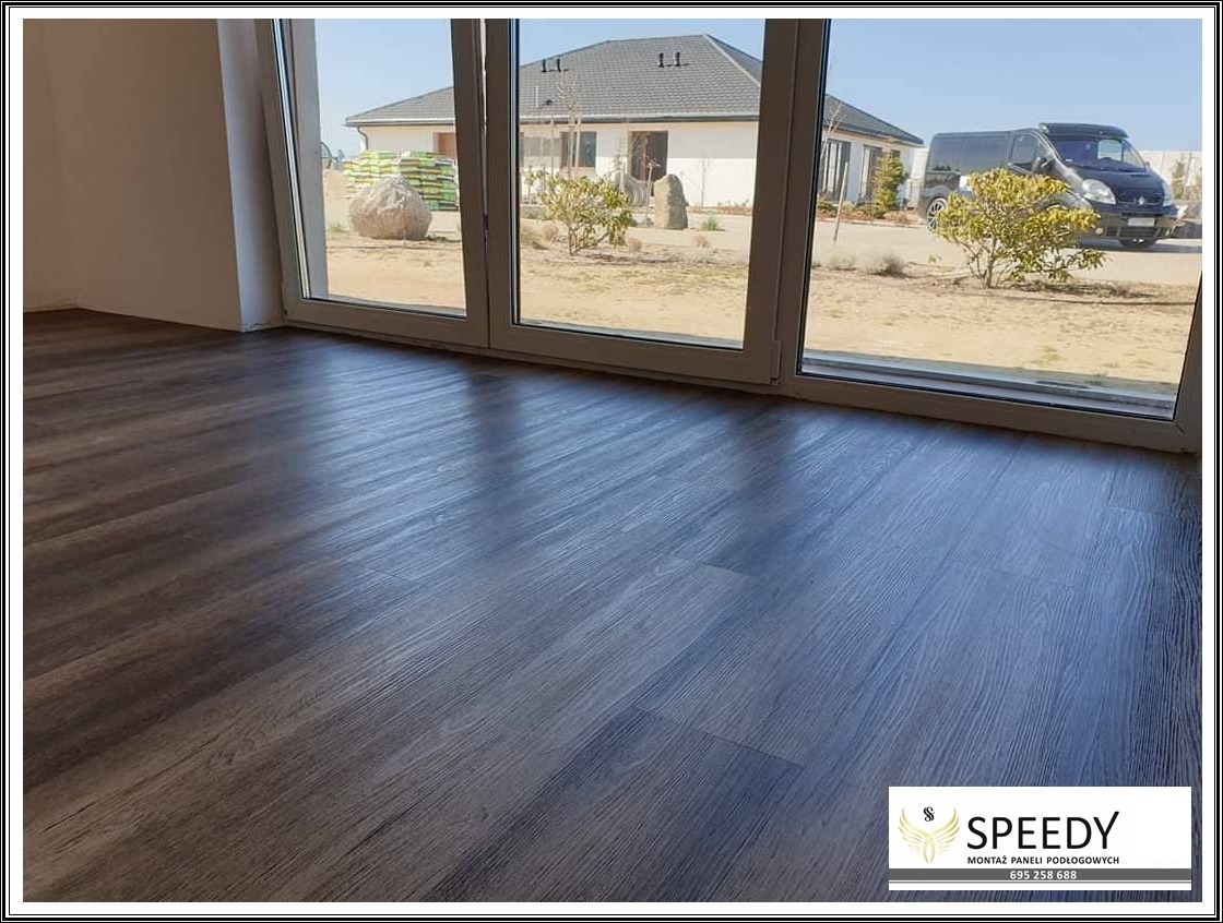 Ułożone panele podłogowe z widokiem na dom jednorodzinny przez duże okno tarasowe.