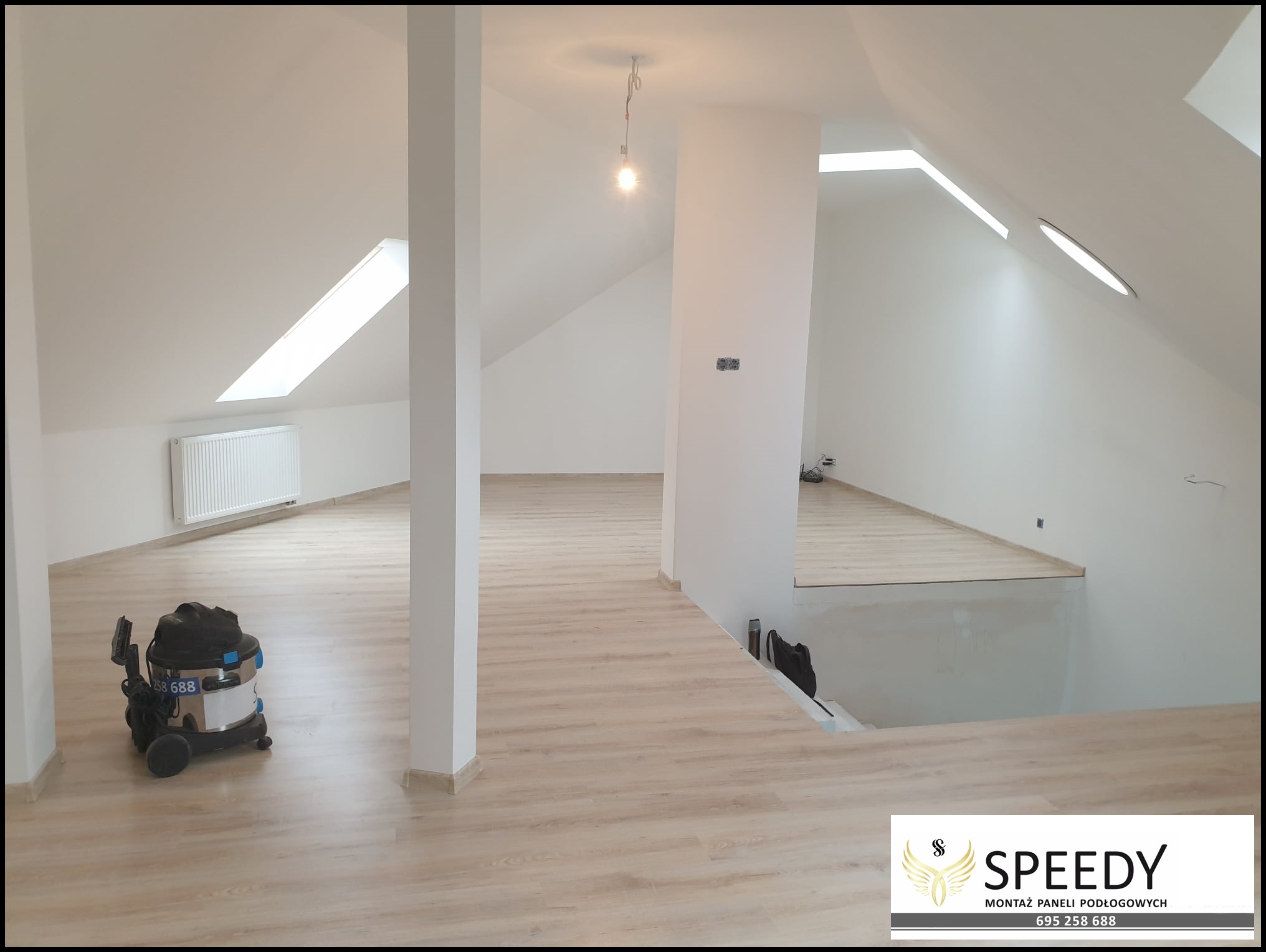 Jasne panele podłogowe ułożone na poddaszu z oknami dachowymi, widoczny odkurzacz przemysłowy i nieukończone schody.