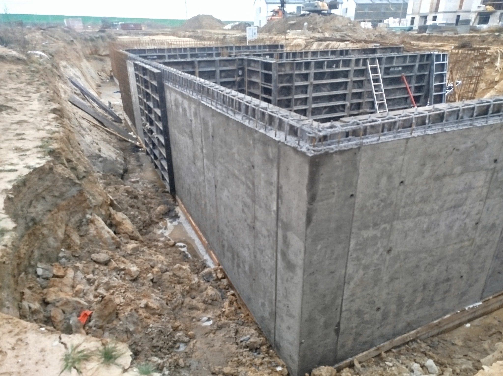 Betonowe fundamenty zbrojone stalą, widoczne szalunki i wykop. Etap budowy domu jednorodzinnego, teren budowy z ziemią i gruzem.