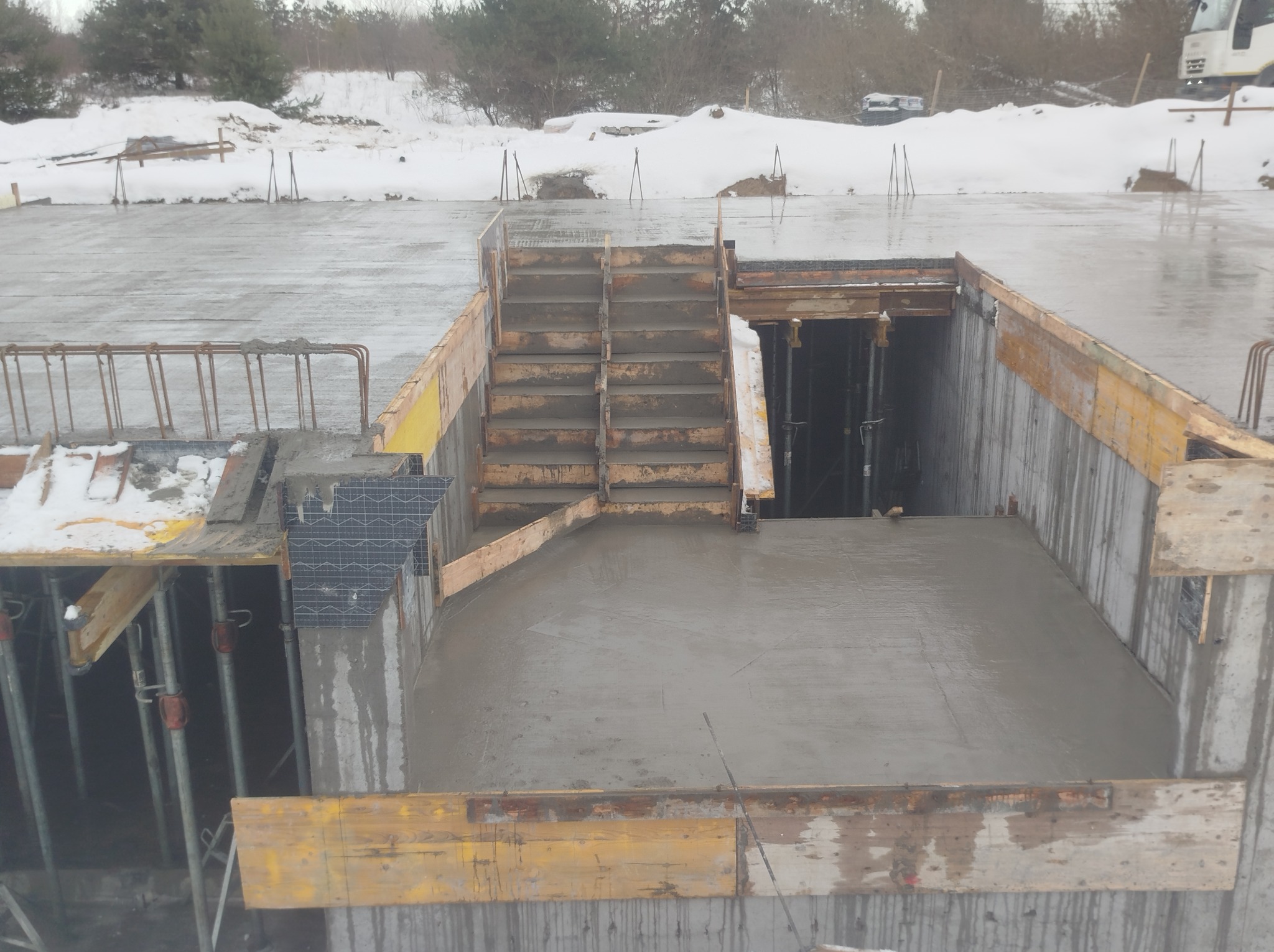 Wylany beton na schody i podest w szalunku, widoczne podpory i zbrojenie. Zimowy krajobraz w tle. Surowy stan budowy.
