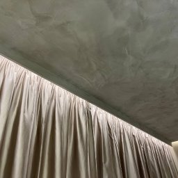 Decor Home - Szara sufitowa powierzchnia z efektem dekoracyjnym, sąsiadująca z kremowymi, marszczonymi zasłonami, widziana z dołu.