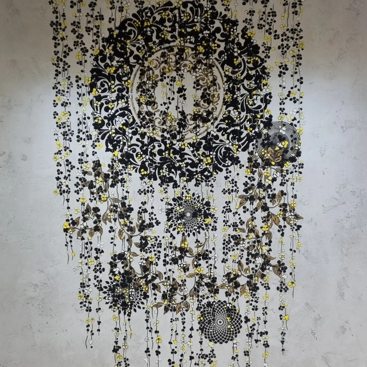 Dekoracyjna ściana z motywem roślinnym w odcieniach czerni, bieli i żółci na szarym, teksturowanym tle.