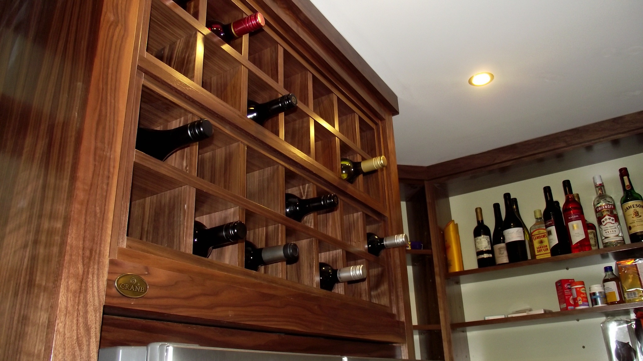 Drewniana szafka na wino z butelkami, wbudowana w kuchnię, z widocznym logo 'Crane' na boku.