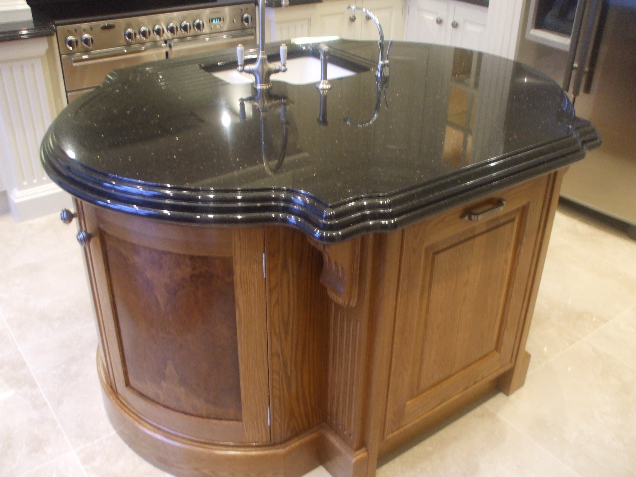 Wyspa kuchenna z ciemnym, błyszczącym blatem z granitu i drewnianą obudową z szafkami w klasycznym stylu, widoczna armatura zlewozmywakowa.