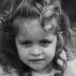 Natalia Kożuch fotografia - Portret czarno-biały dziewczynki z burzą kręconych włosów, skierowanej w stronę obiektywu, z delikatnym uśmiechem.