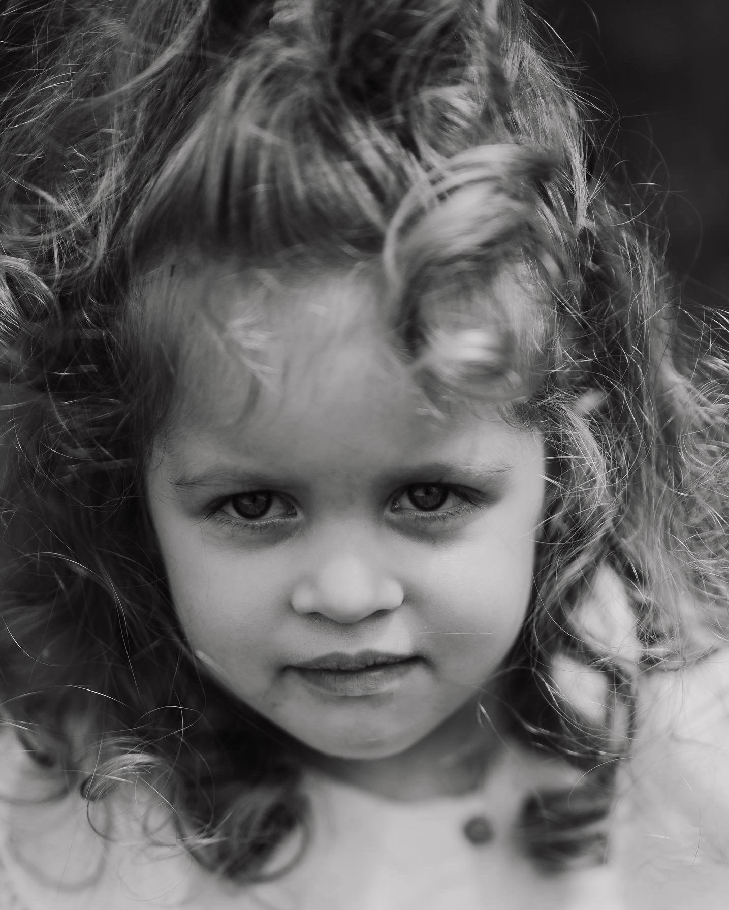 Portret czarno-biały dziewczynki z burzą kręconych włosów, skierowanej w stronę obiektywu, z delikatnym uśmiechem.