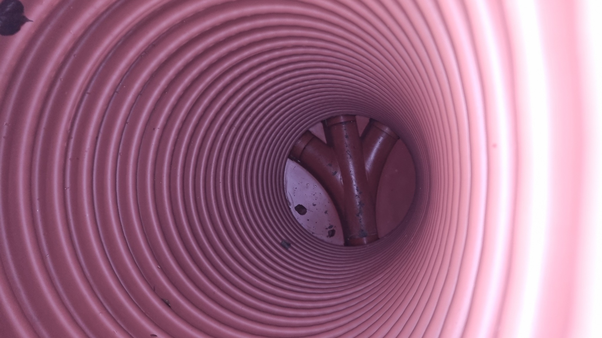 Wnętrze karbowanej rury kanalizacyjnej z trójnikiem z tworzywa sztucznego. Widok z perspektywy wnętrza rury, ukazujący połączenie.