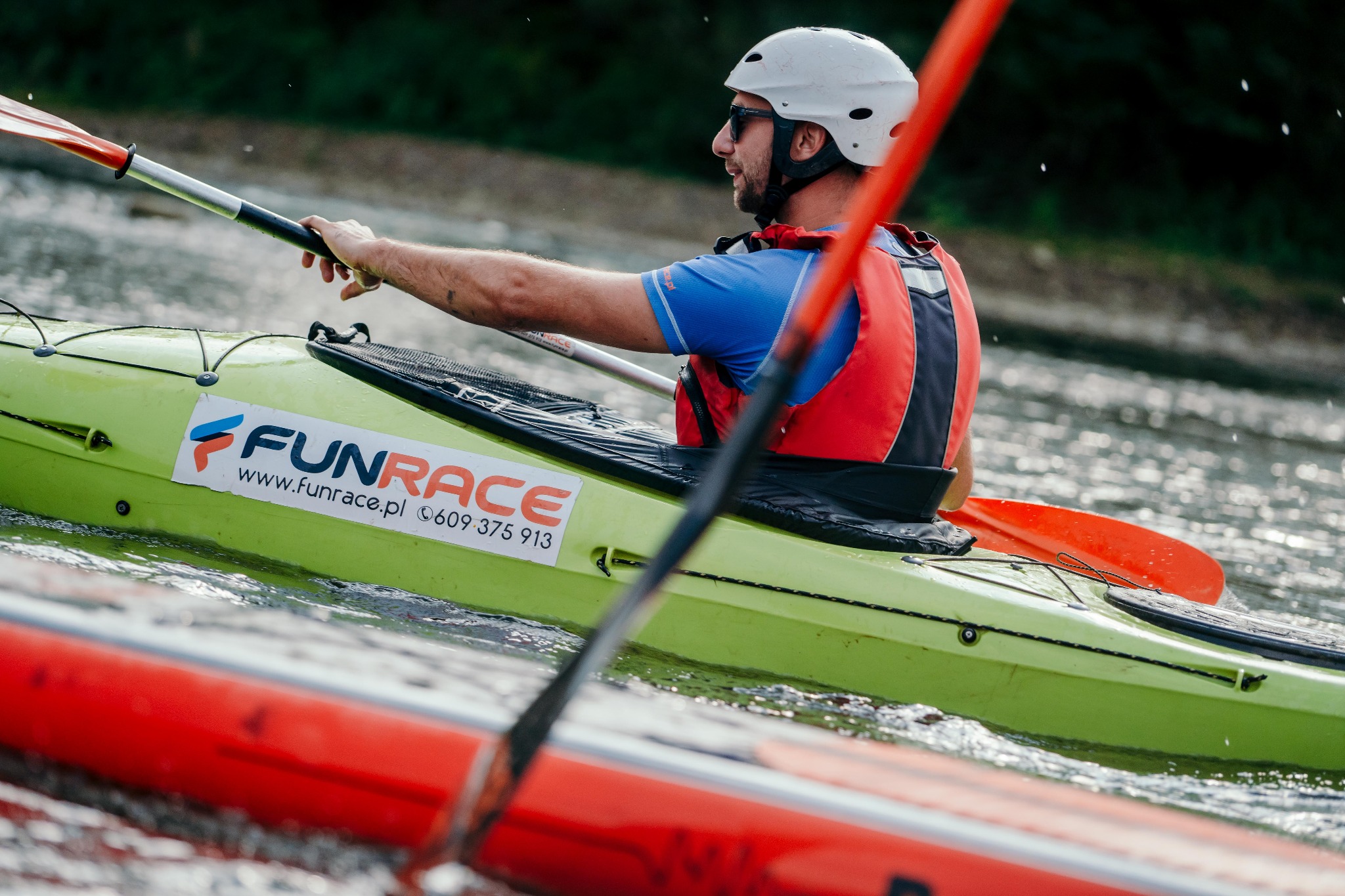 Mężczyzna w kasku i kamizelce asekuracyjnej wiosłuje kajakiem marki FunRace po rzece.