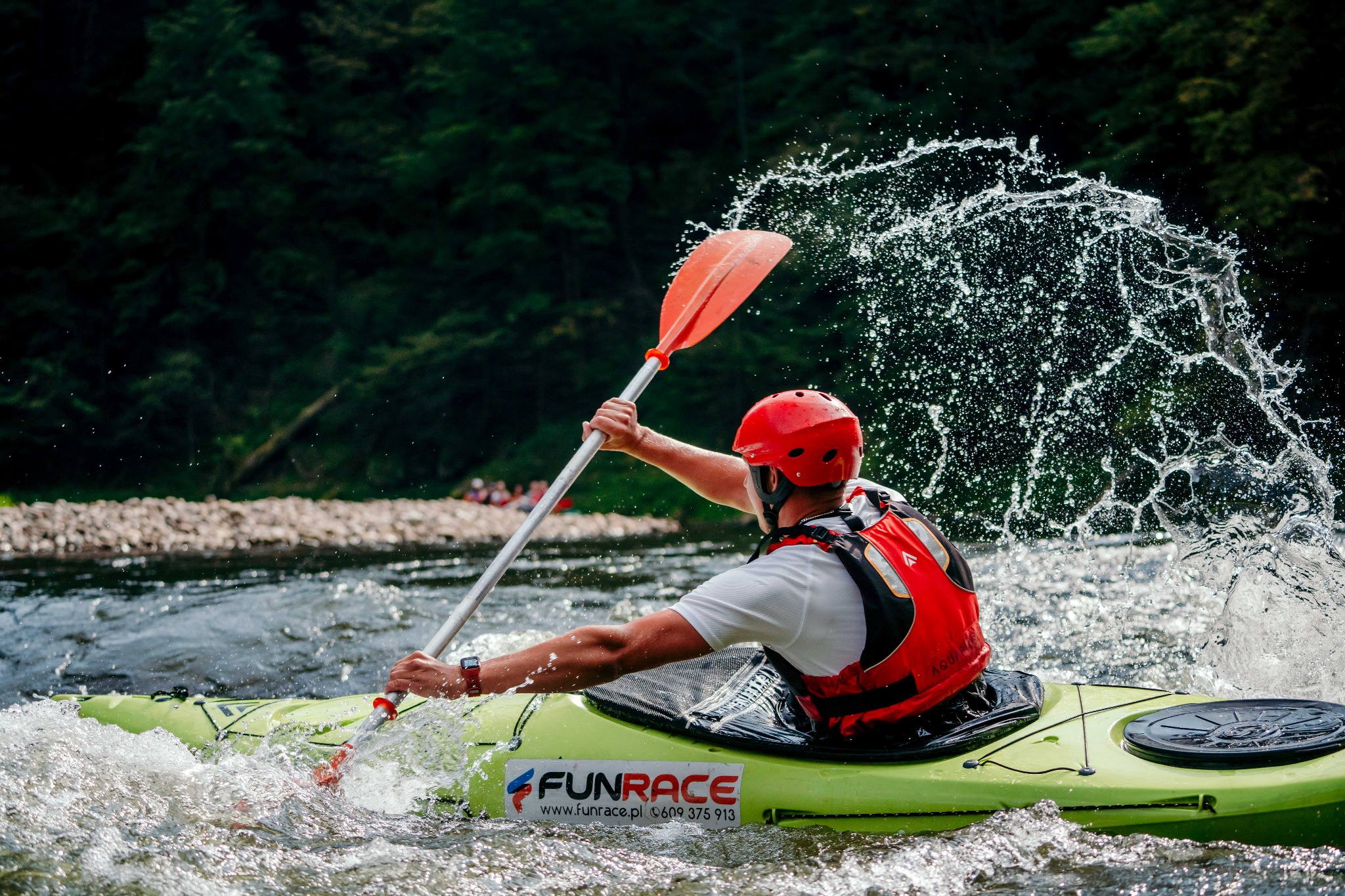 Kajakarz w czerwonym kasku i kamizelce wiosłuje pomarańczowym wiosłem, wzbijając fontannę wody; na zielonym kajaku widoczne logo FunRace.
