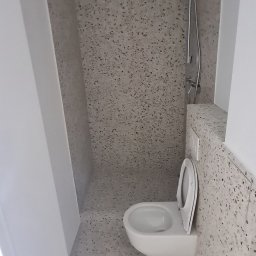 Radosław Kefer - Nowoczesna łazienka z toaletą podwieszaną i prysznicem, wykończona płytkami imitującymi lastryko na ścianach i podłodze, z minimalistyczną armaturą.