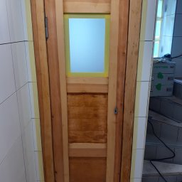 Radosław Kefer - Drewniane drzwi z szybą, zabezpieczone taśmą malarską na styku z białą, kwadratową glazurą, w tle widoczny sprzęt Festool.