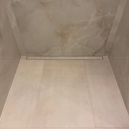 Radosław Kefer - Beżowe płytki podłogowe i marmuropodobne płytki ścienne w kabinie prysznicowej z odpływem liniowym.