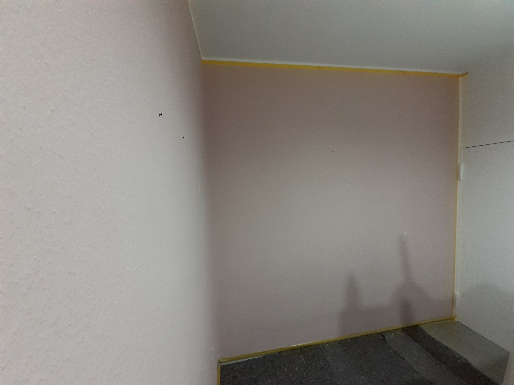 Przygotowane do malowania wnętrze pokoju z różowymi ścianami zabezpieczonymi żółtą taśmą malarską przy suficie i podłodze.