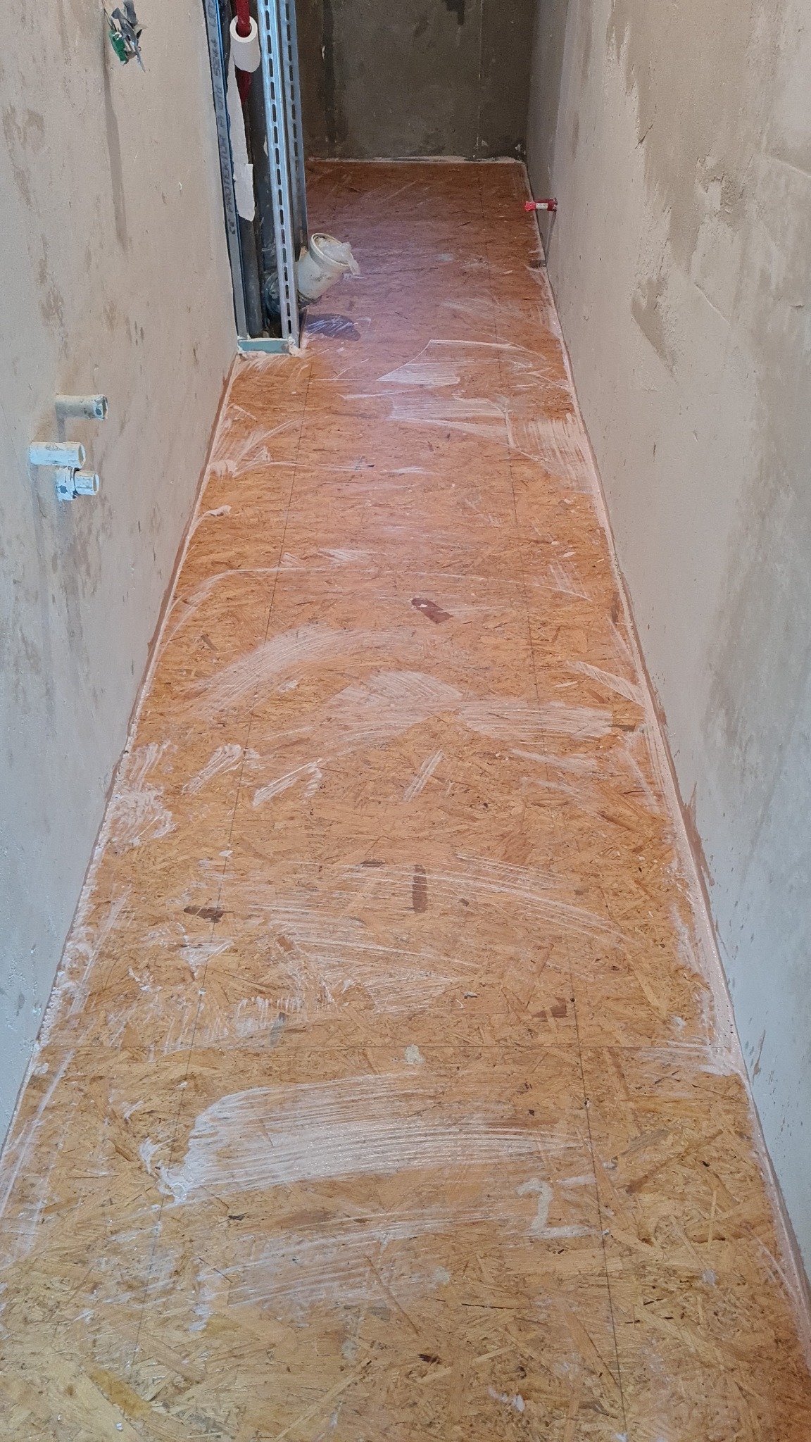 Przygotowanie podłoża z płyt OSB w wąskim korytarzu, gruntowanie białą emulsją, ściany w stanie surowym.