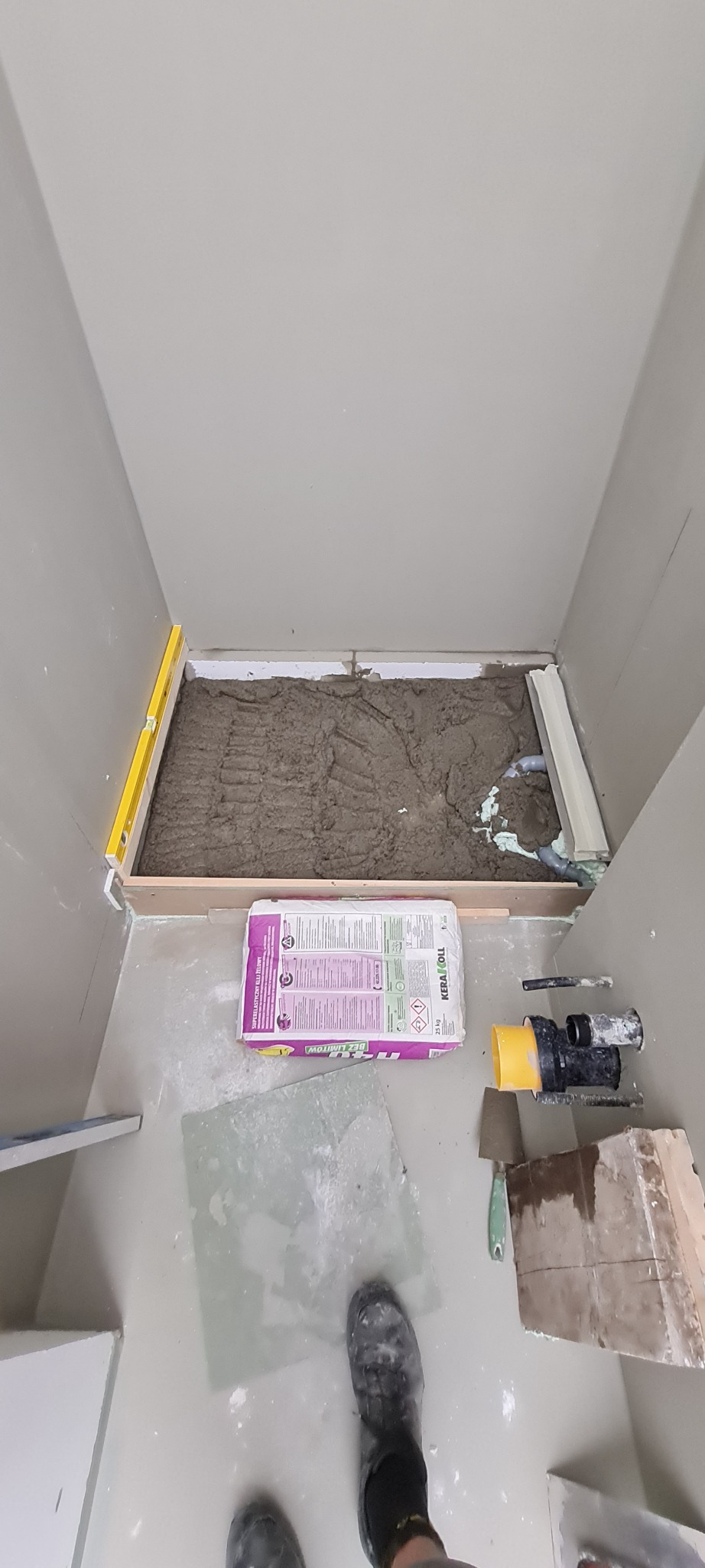 Przygotowanie podłoża pod prysznic z wylewką i workiem kleju elastycznego KeraKoll Bez Limitu, widoczne narzędzia i poziomica.