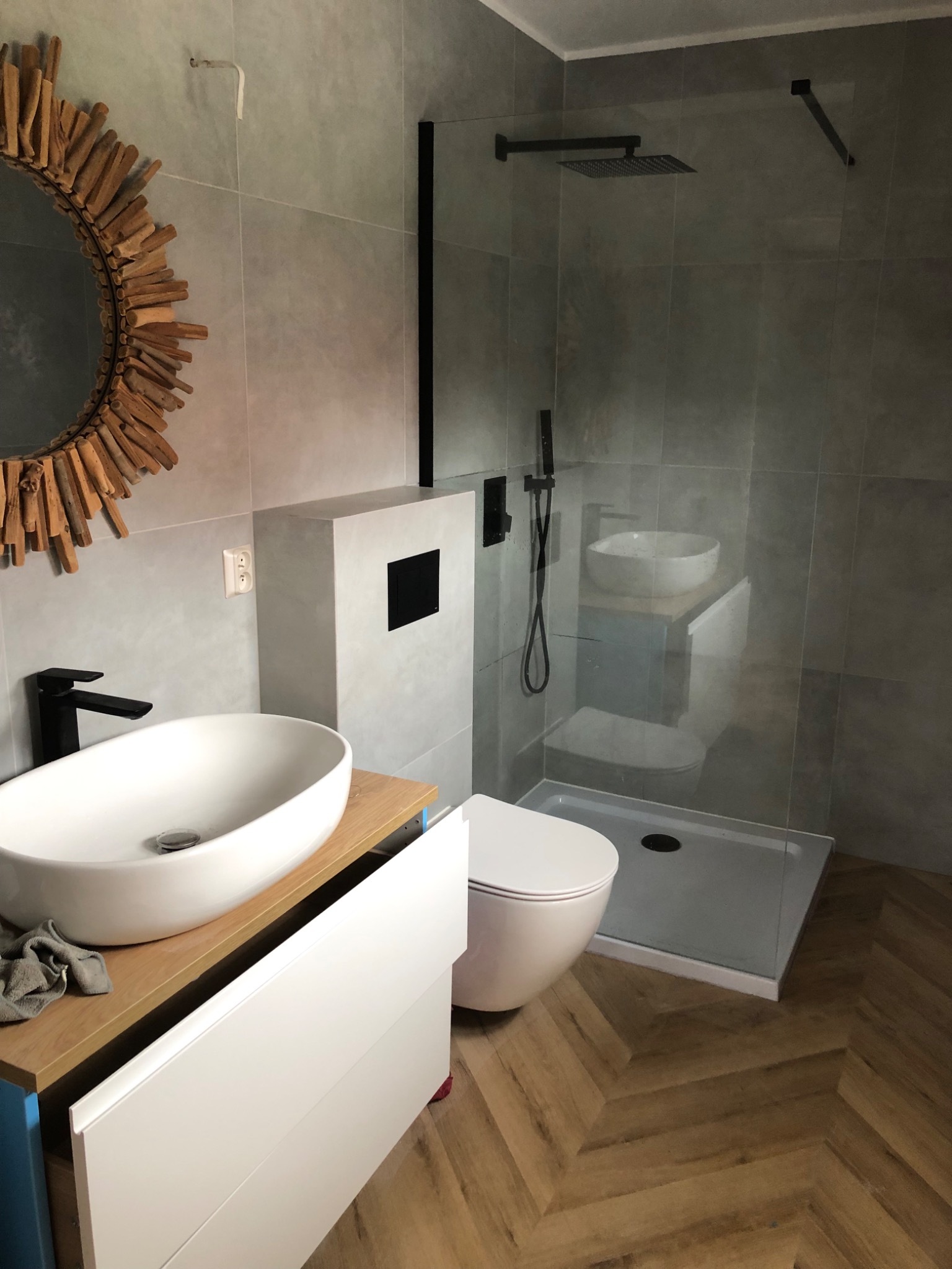 Nowoczesna łazienka z kabiną typu walk-in, umywalką nablatową na drewnianym blacie i lustrem w drewnianej ramie. Na podłodze panele ułożone w jodełkę.