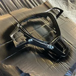 Element kierownicy samochodowej po lakierowaniu na czarno, leżący na zabezpieczonej folią i kartonem powierzchni, widoczne drobne niedoskonałości lakieru.