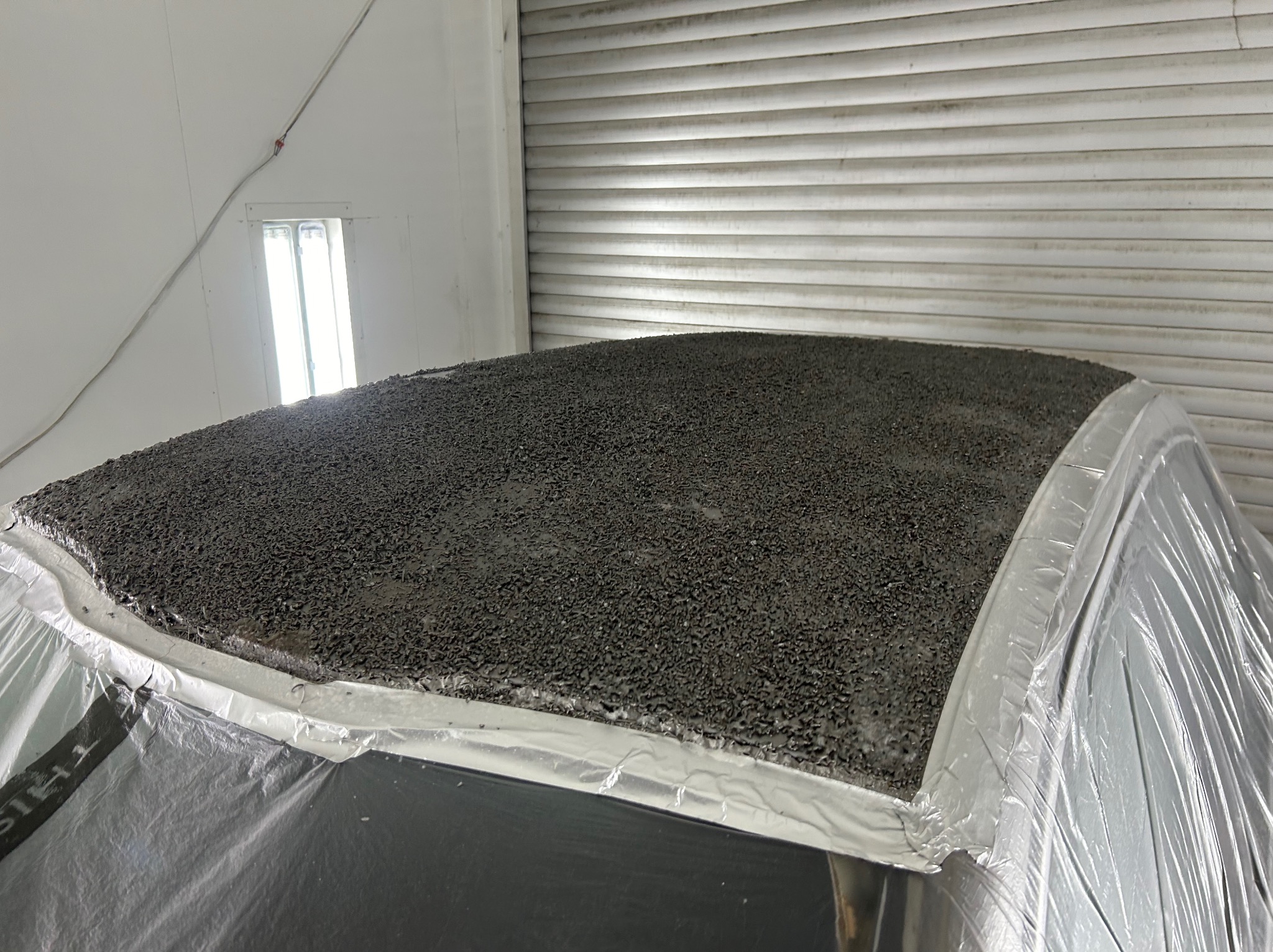 Dach samochodu pokryty grubą warstwą szpachli, przygotowany do dalszej obróbki, zabezpieczony folią malarską, w tle brama garażowa.