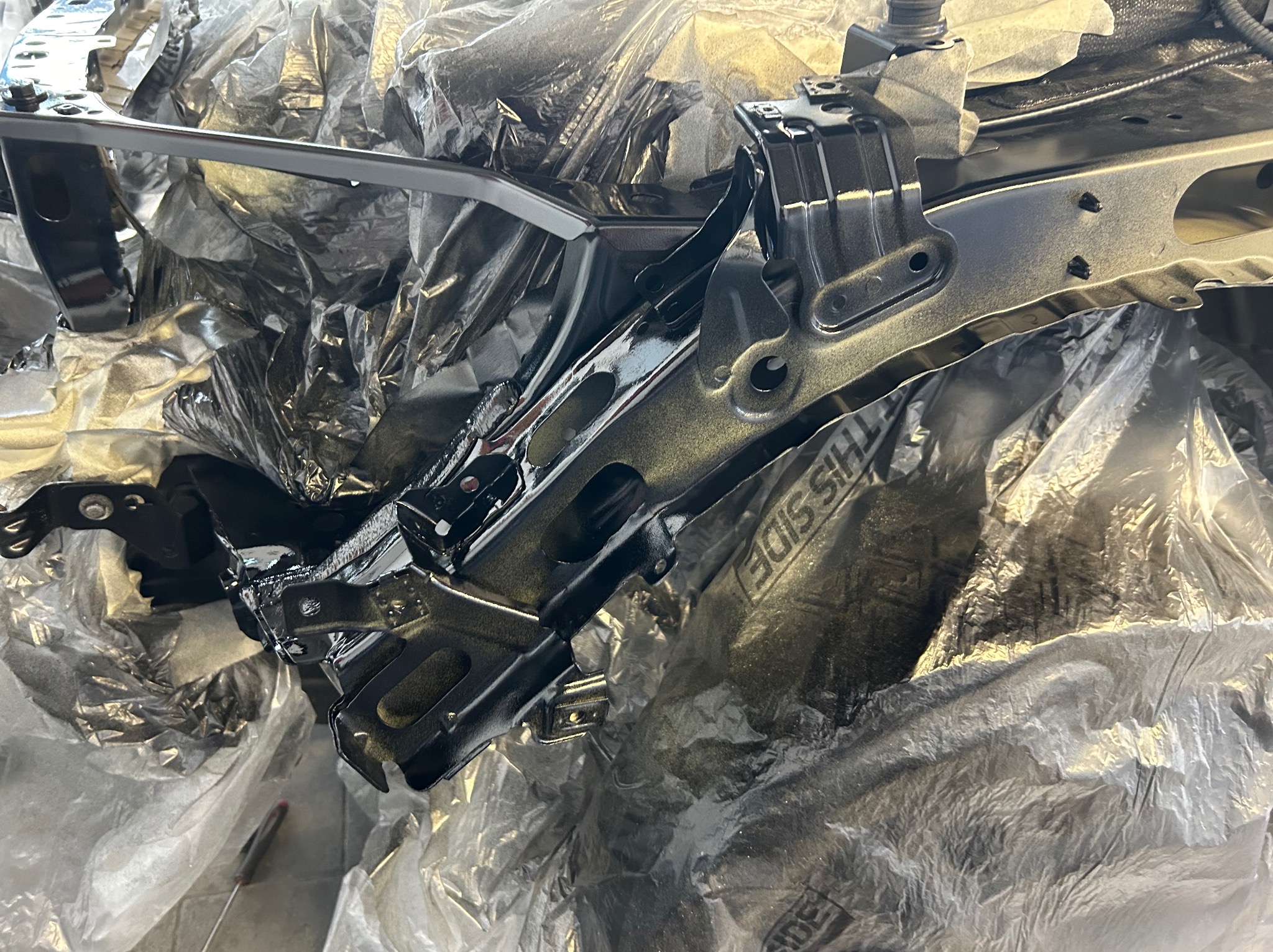 Świeżo polakierowany, czarny element karoserii samochodowej, zabezpieczony folią, w warsztacie w Siemianowicach Śląskich. Widoczne ślady lakieru na folii ochronnej i narzędzie w tle.