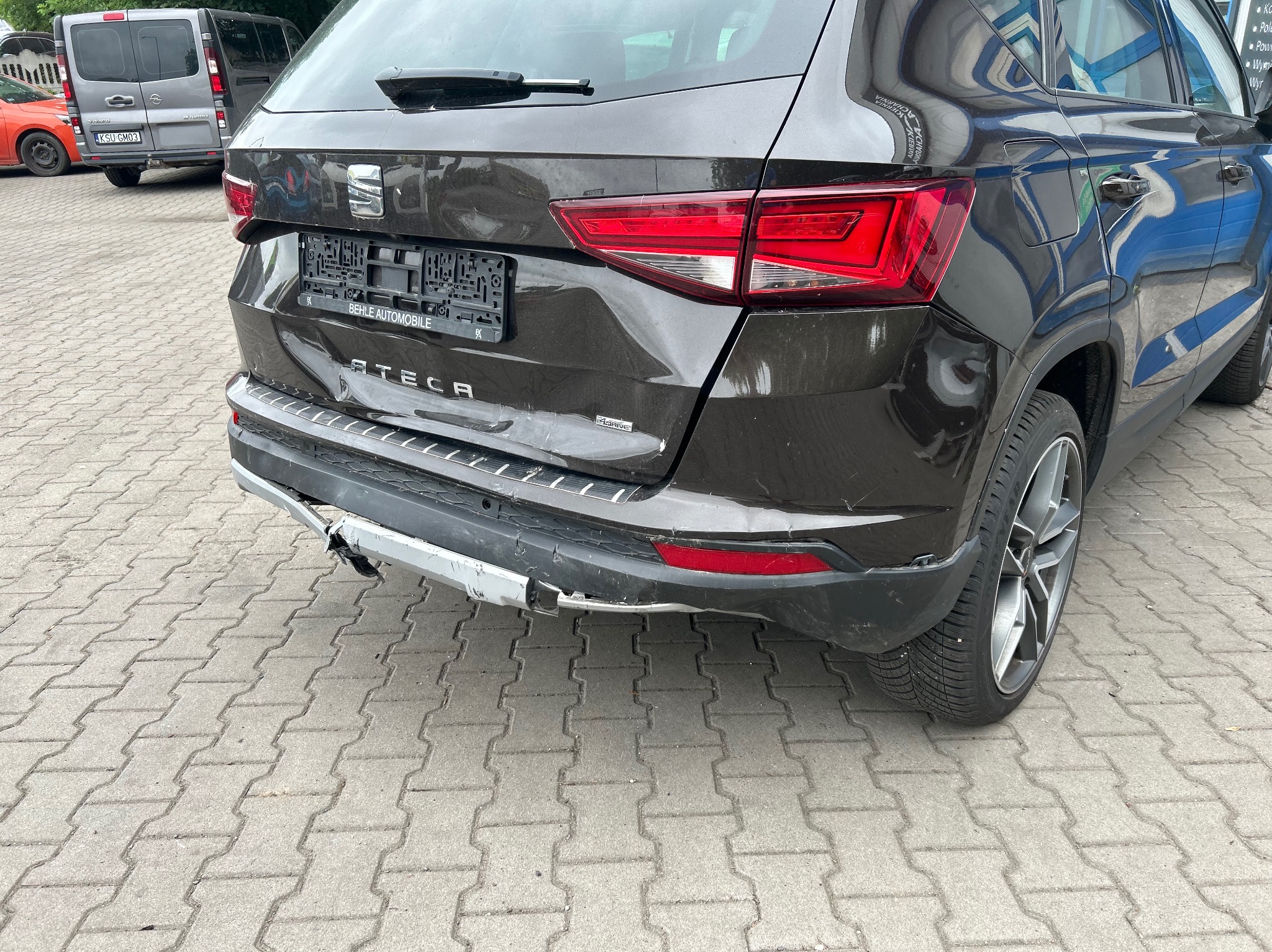 Uszkodzony tylny zderzak brązowego samochodu Seat Ateca, widoczne wgniecenia i odkształcenia blachy, fragment srebrnego elementu zderzaka oderwany.