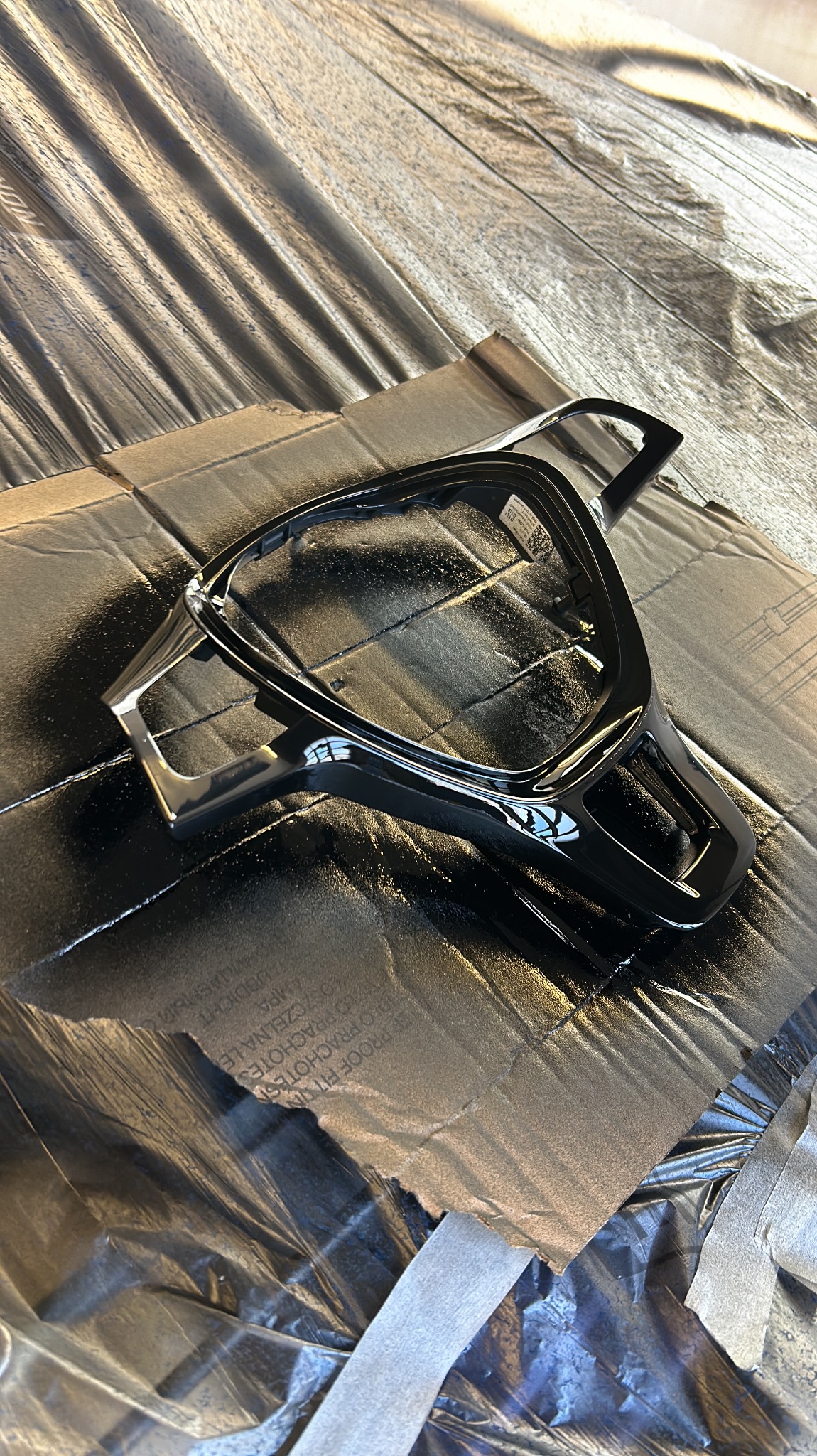 Element kierownicy samochodowej po lakierowaniu na czarno, leżący na zabezpieczonej folią i kartonem powierzchni, widoczne drobne niedoskonałości lakieru.