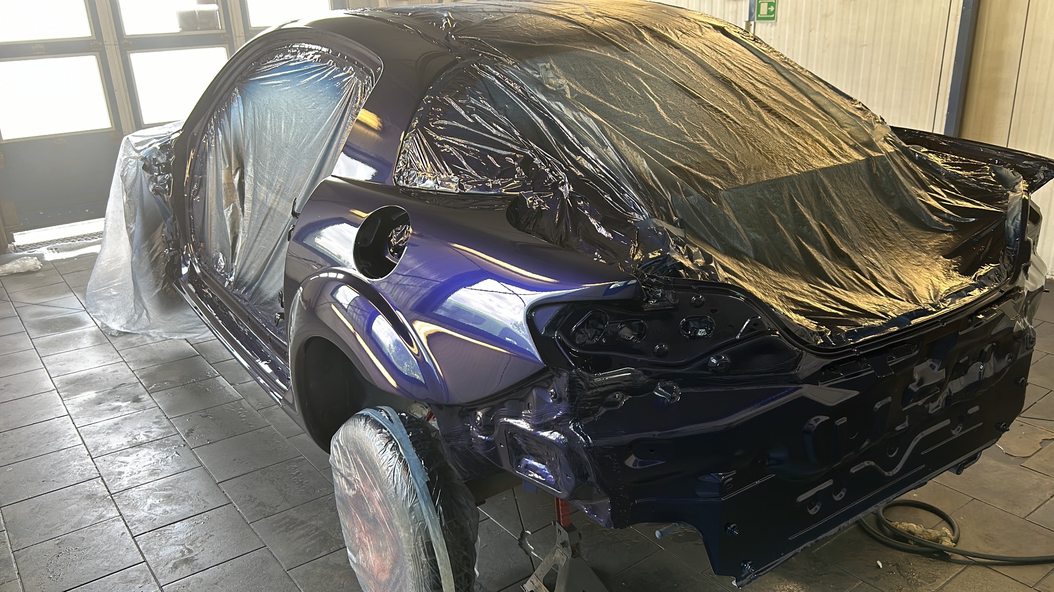 Samochód w trakcie lakierowania na kolor granatowy, częściowo zakryty folią ochronną w warsztacie.