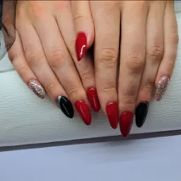 Dłonie z pomalowanymi paznokciami w kolorach czerwonym, czarnym i srebrnym brokatem, kształt szpiczasty na białym tle.