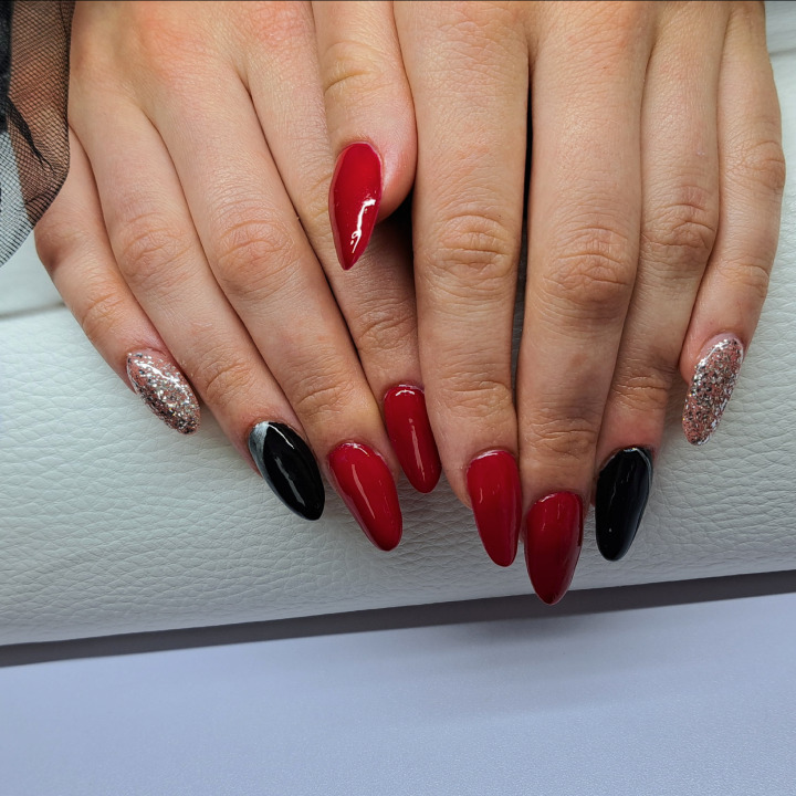 Dłonie z pomalowanymi paznokciami w kolorach czerwonym, czarnym i srebrnym brokatem, kształt szpiczasty na białym tle.