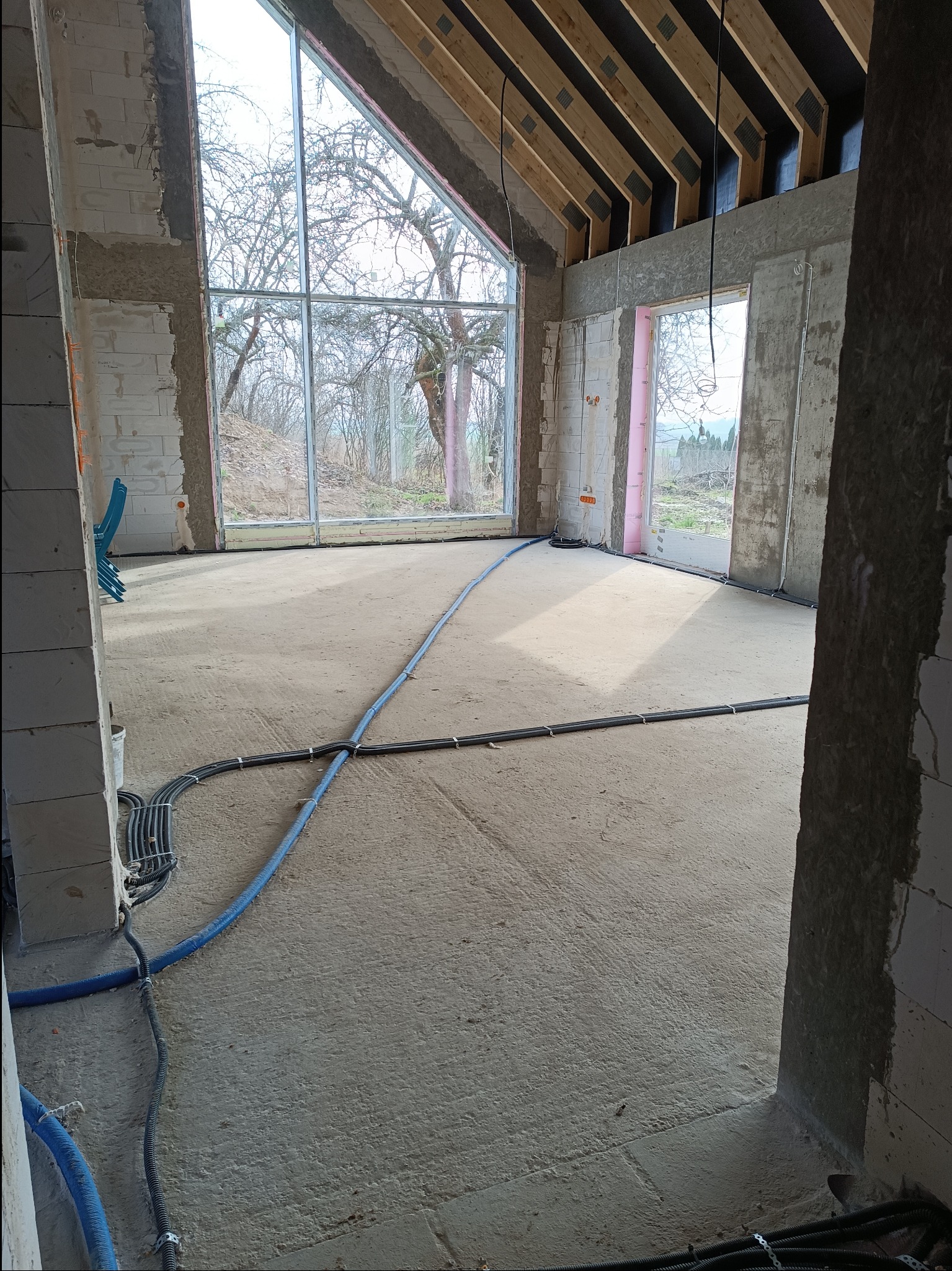 Wnętrze w stanie surowym z widocznymi przewodami elektrycznymi prowadzonymi po podłodze, przygotowane do dalszych prac wykończeniowych.