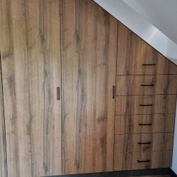 BARTOSZ MROCZEK BARTMEB - Zabudowa wnęki na poddaszu z drewnopodobnymi frontami, czarnymi uchwytami i czterema szufladami, dopasowana do skosu dachu.