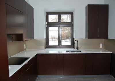 Nowoczesna kuchnia z ciemnobrązowymi szafkami, białym blatem i czarną armaturą, widok na zimowy krajobraz za oknem.