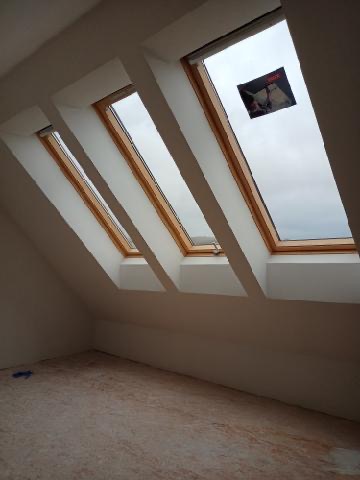 Poddasze z trzema oknami dachowymi, ściany przygotowane do malowania, widoczne ślady szpachlowania na podłodze.